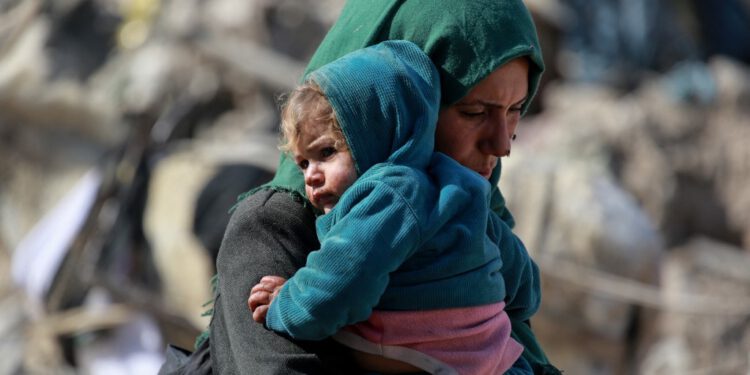 Eine palästinensische Frau trägt ein Baby, während Familien nach israelischen Luftangriffen in den frühen Morgenstunden des 18. März 2025 auf den Norden und andere Teile des Gazastreifens den östlichen Teil des Gazastreifens an der Grenze zu Israel verlassen. Die israelische Armee forderte die Bewohner Gazas am 18. März auf, Gebiete in der Nähe der Grenze zu evakuieren, nachdem sie in der Nacht eine Welle tödlicher Angriffe gestartet hatte, die intensivsten seit Beginn der Waffenruhe im Januar. Die Rettungskräfte von Gaza gaben an, dass die Zahl der Todesopfer durch die massive israelische Offensive im gesamten palästinensischen Gebiet auf über 220 Menschen, darunter auch Kinder, gestiegen sei. (Foto: Bashar TALEB / AFP)