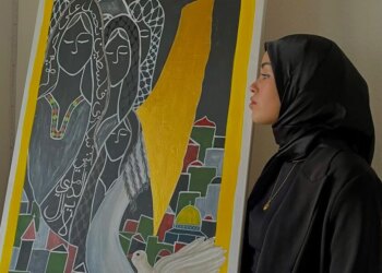 Frau mit schwarzem Kopftuch im Profil neben einem Gemälde mit Frauengesichtern